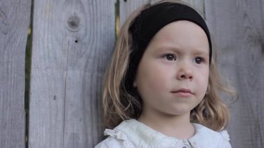 Ahşap bir çit arka plan karşı duran bir siyah bandana ile mavi elbiseli kıvırcık saçlı kız