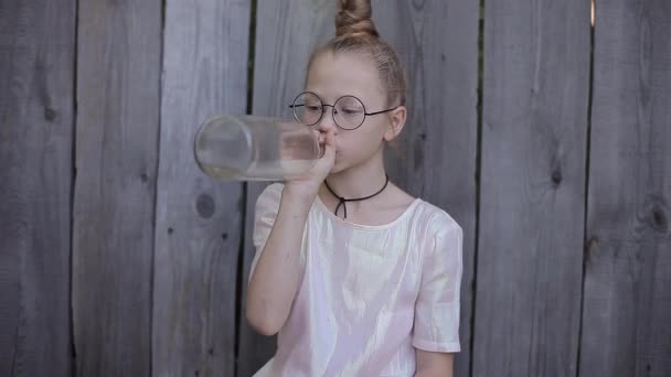 Jeune fille avec verres ronds boit de l'eau à partir de bouteilles en verre et souriant — Video