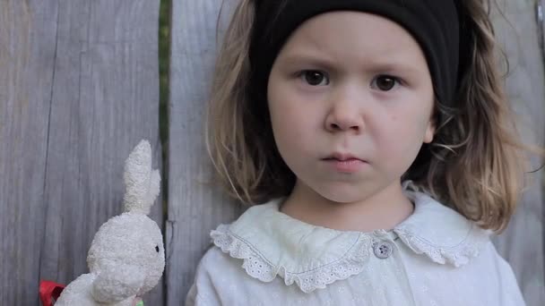 Serious Little Curly Girl con ojos tristes sostiene un conejo de juguete y mira a la cámara — Vídeo de stock