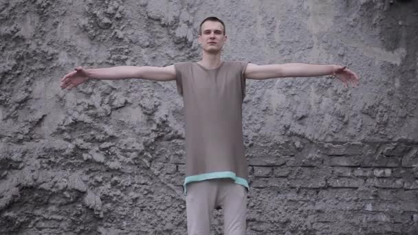 Un hombre con una ropa futurista gris de pie con los brazos abiertos en el fondo de la pared de ladrillo — Vídeos de Stock