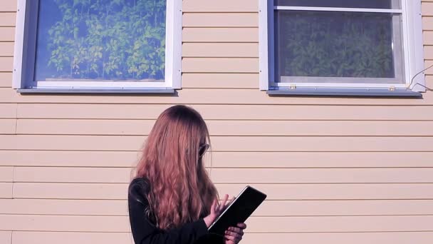 Menina no fundo da casa com janelas em óculos de sol com tablet — Vídeo de Stock