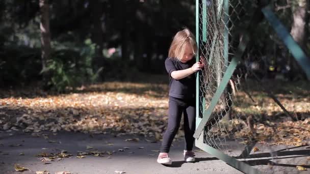 Little Cute Girl próbuje otworzyć siatki bramy i przejrzeć je i mówi coś — Wideo stockowe