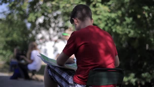 Un garçon en T-shirt rouge peint un tableau en plein air — Video