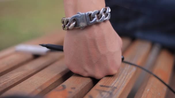 Man's Hand met een ijzeren ketting armband met een zwarte Marker rusten op de houten bank — Stockvideo