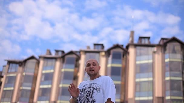 Schöner weißer Mann, der vor dem Hintergrund mehrstöckiger Gebäude und sonnigen Himmels rappt — Stockvideo