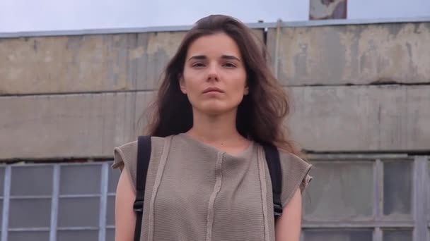 Bella ragazza con i capelli castani in piedi sullo sfondo dell'edificio industriale — Video Stock