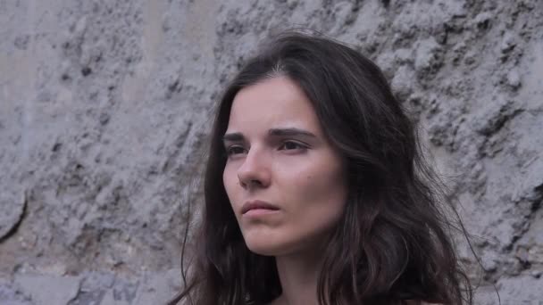 Vue de côté : Une belle jeune brune célibataire se tient contre le mur industriel post-apocalyptique — Video