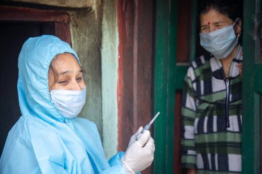 PPE koruyucu maskeli genç kadın doktor elinde şırınga ve koronavirüs aşısı tutan eldivenler, köy kadınlarıyla birlikte durup Corona virüsü aşısının önemini anlatıyor. Hastalığa karşı yeni bir aşı konsepti, grip aşısı.