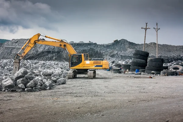 Pesada excavadora con pala de pie en la colina con rocas —  Fotos de Stock