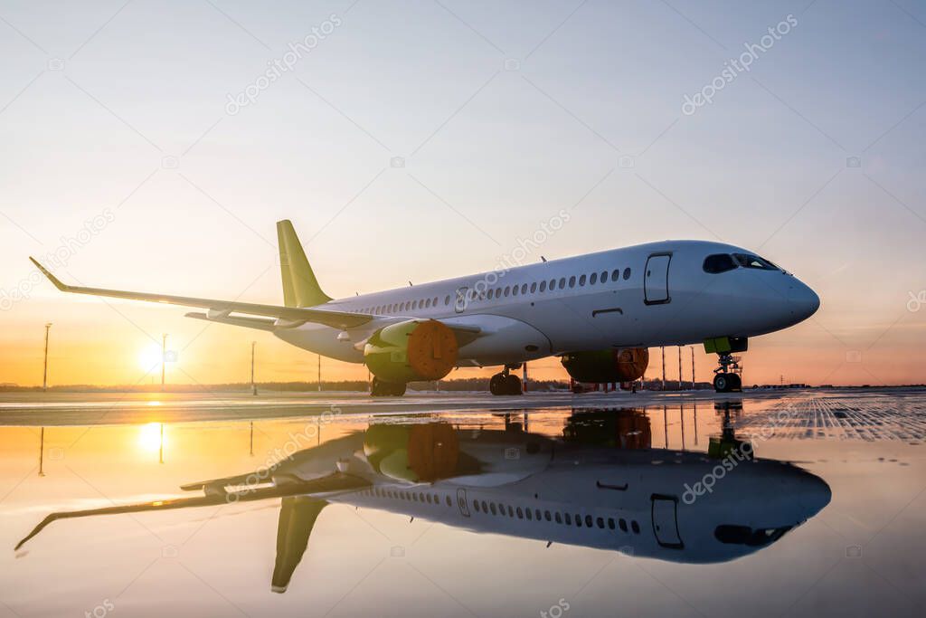 Modern passenger airplane on the apron of the airport against the backdrop of a picturesque sunset with reflection in a puddle