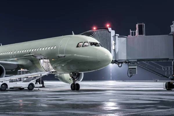 Yolcu uçağı bir havaalanı gece önlüğüyle jetway 'de duruyor. Uçağın bagaj bölümü açık ve bavullar yükleniyor.