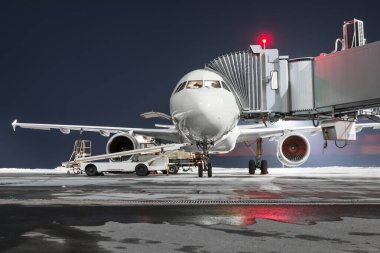 Yolcu uçağının ön görüntüsü gece havaalanı önlüğünün üzerinde duruyor. Uçağın bagaj bölümü açık ve bavullar yükleniyor.