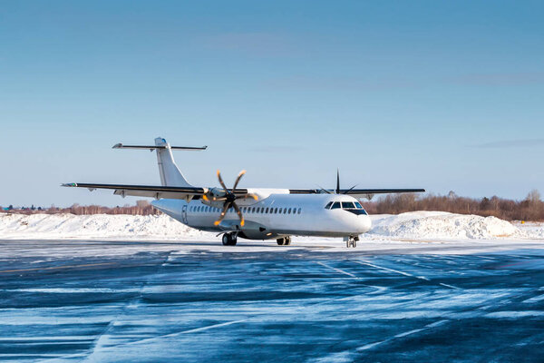 Белый пассажирский турбовинтовой авиалайнер на фартуке аэропорта в холодную зимнюю погоду