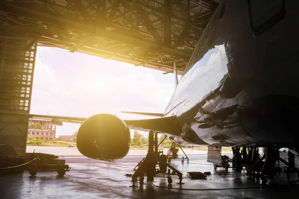 Beyaz yolcu uçağı hangarda bakım altında. Jet uçağının onarımı ve uçuş işlemleri için mekanik sistemler kontrol ediliyor