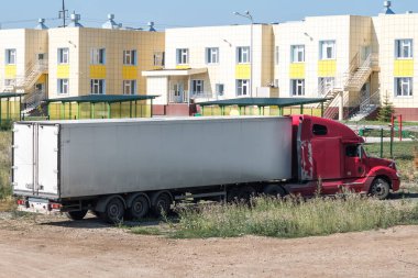 Kırsal kesimde beyaz yarı karavanı olan kırmızı uzun mesafe kaput kamyonu.
