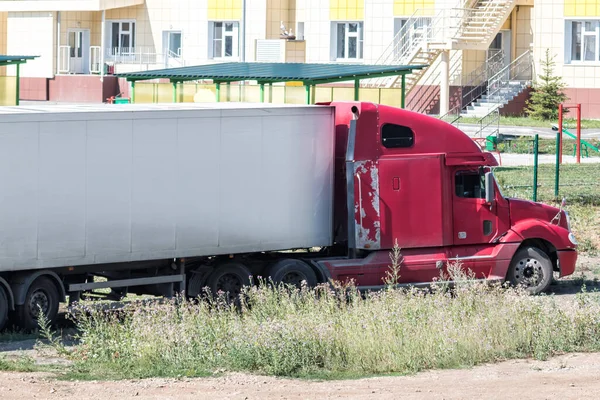 Red long-distance bonnet truck with a white semitrailer in the countryside