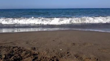 Kumsalın yakın görüntüsü: Her dönen dalgada kum taneleri kayarken, ıslak yüzey boyunca köpük dantelli, geçici desenler, küçük çıkıntıları ve çizgileri yeniden düzenliyor.