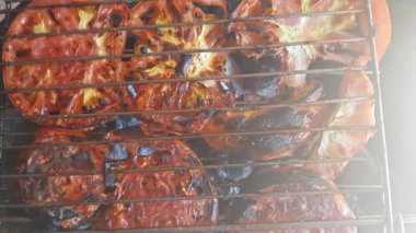 Kömürde kızartılmış domates dilimleri, derileri kabarmış ve bazı yerlerde kararmış. Dilimler arasında duman sürükleniyor, dumanlı bir tatlılık ve lezzet yayıyor.