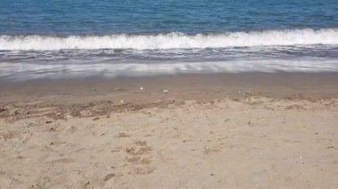 Sahilin manzarası, kıyı hafif dalgalar halinde soluyor. Küçük dalgalar köpüğe dönüşür ve her gelgitte ritmik bir sessizlik gelir ve gider..