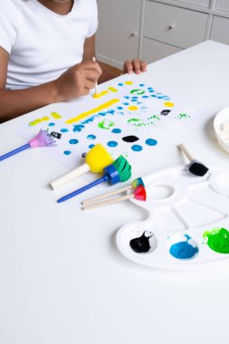Child painting with sponges and brushes on white table. High quality.