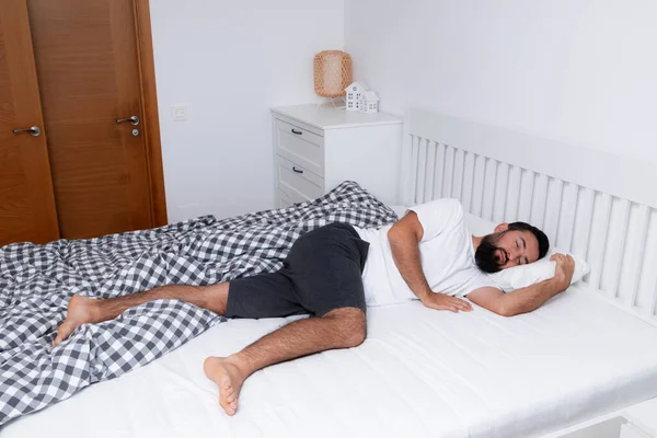 Genç beyaz erkek, minimalist yatak odasındaki beyaz yatakta huzur içinde uyuyor. Yüksek kalite.