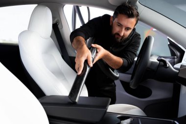 Latin kökenli genç bir erkek siyah kazakla arabanın içini süpürüyor. Yüksek kalite.