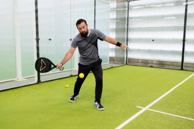 Genç İspanyol erkek, yeşil sahada içeride raket oynuyor. Yüksek kalite.