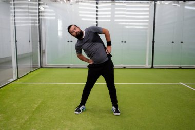 Beyaz erkek antrenman yapıyor. Kapalı sahada esneme hareketleri. Yüksek kalite.