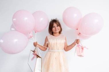 Parti elbisesi içinde elinde pembe balonlar ve hediye taşıyan Asyalı bir kadın çocuk. Yüksek kalite.