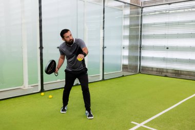 Yetişkin bir erkek, yeşil sahada kapalı alanda tenis oynuyor. Yüksek kalite.