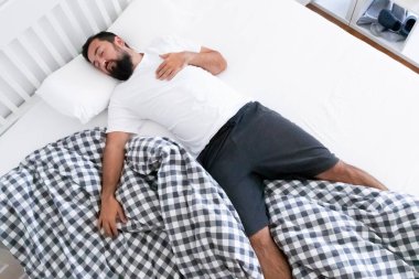 Rahat, genç, beyaz erkek rahat bir şekilde rahat bir şekilde yatakta uyuyor. Yüksek kalite.