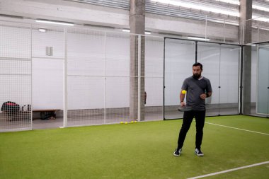 Erkek bir yetişkin, kapalı sahada raket ve topla padel antrenmanı yapıyor. Yüksek kalite.