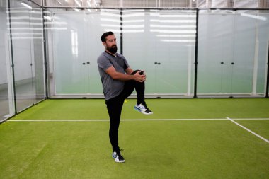 Atletik yetişkin beyaz erkek, kapalı spor sahasında bacak esnetiyor. Yüksek kalite.