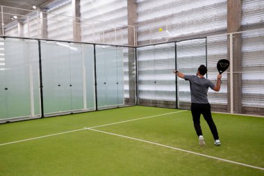 Erkek, yeşil sahada kapalı alanda Padel tenis oynuyor. Yüksek kalite.