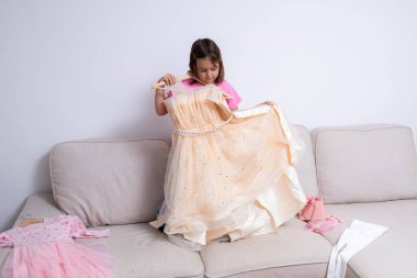 Kafkasyalı genç bir kız evdeki kanepede ışıltılı elbiseye hayran. Yüksek kalite.