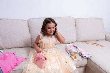 Parlak elbiseli, telefonda konuşan ve elinde hediye çantası olan beyaz bir kız çocuğu. Yüksek kalite.