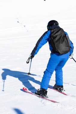 Kar yamacında mavi kıyafetli ve sırt çantalı biri kayak yapıyor. Yüksek kalite.
