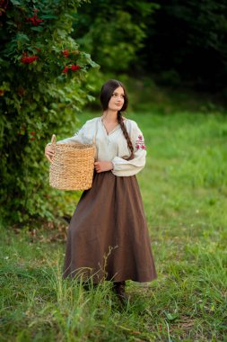 Geleneksel Ukrayna kıyafetleriyle uzun siyah örgülü güzel esmer kadın yeşil arka planda parlak kırmızı viburnum ile poz veriyor, çarpıcı bir portre, canlı bir açık hava sahnesi..