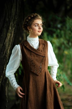 Sarışın, zarif saç stiline sahip, güzel, klasik elbiseli, bisiklet süren, doğal bir ortamda poz veren, zamansız moda, zarafet ve çarpıcı detaylarla dolu yumuşak, rüya gibi bir atmosferi olan bir kadın.