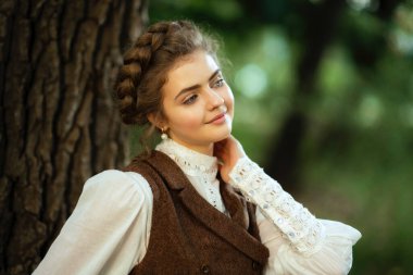 Sarışın, zarif saç stiline sahip, güzel, klasik elbiseli, bisiklet süren, doğal bir ortamda poz veren, zamansız moda, zarafet ve çarpıcı detaylarla dolu yumuşak, rüya gibi bir atmosferi olan bir kadın.