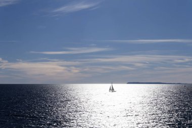 Small Sailboat Sailing on a Sparkling Sea Horizon Against a Vast Blue Sky