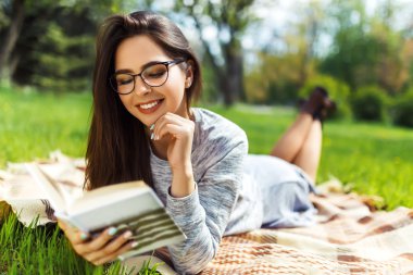 Güzel rahat genç kadın güneş parlayan çim bir kitap okuma. 