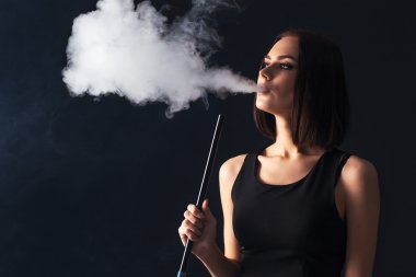 Genç, güzel bir kız bir nargile içiyor. Onun ağzından çıkan duman üretir. İş tarzı giyim. Sigara keyfi.
