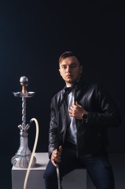 Genç, yakışıklı adam bir nargile sigara. Onun ağzından çıkan duman üretir. İş tarzı giyim. Sigara keyfi.