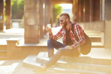 Basamaklarında oturan ve kahve içme hipster adam. genç adam