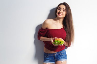 Young beautiful girl with a burger in her hands. Studio shot. Model. Fast food meal