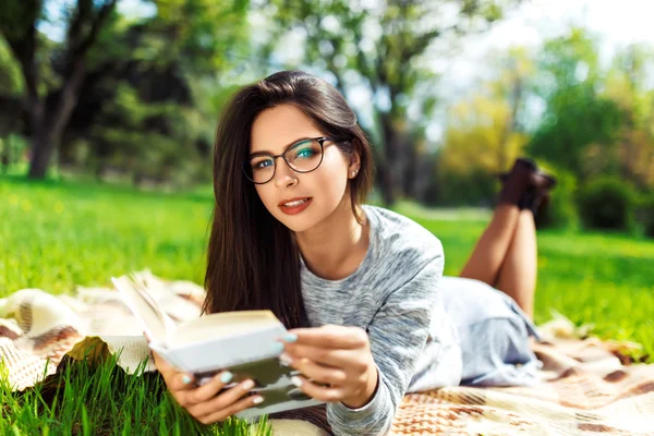 Mooie ontspannen jonge vrouw het lezen van een boek op het gazon met zon schijnt. — Stockfoto