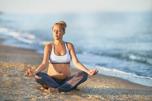 Femme enceinte faisant du yoga sur la plage. Lumière douce. Belle fille avec un maillot de bain. La mer. Elle se relaxe yoga . — Photo