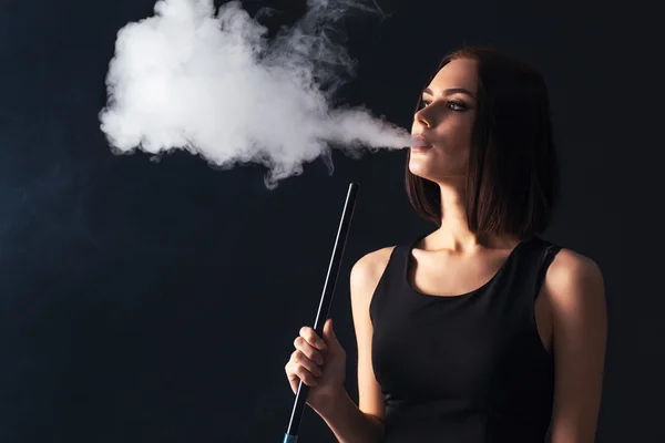 Young, beautiful girl smokes a hookah. It produces smoke from his mouth. Business style clothing. The pleasure of smoking.