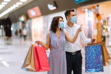 Alışveriş torbaları tutan, vitrinlere bakan ve alışveriş merkezinden alışveriş yapan genç bir çift. Coronavirüs salgınında alışveriş. Satış, tüketim, Kara Cuma konsepti. 